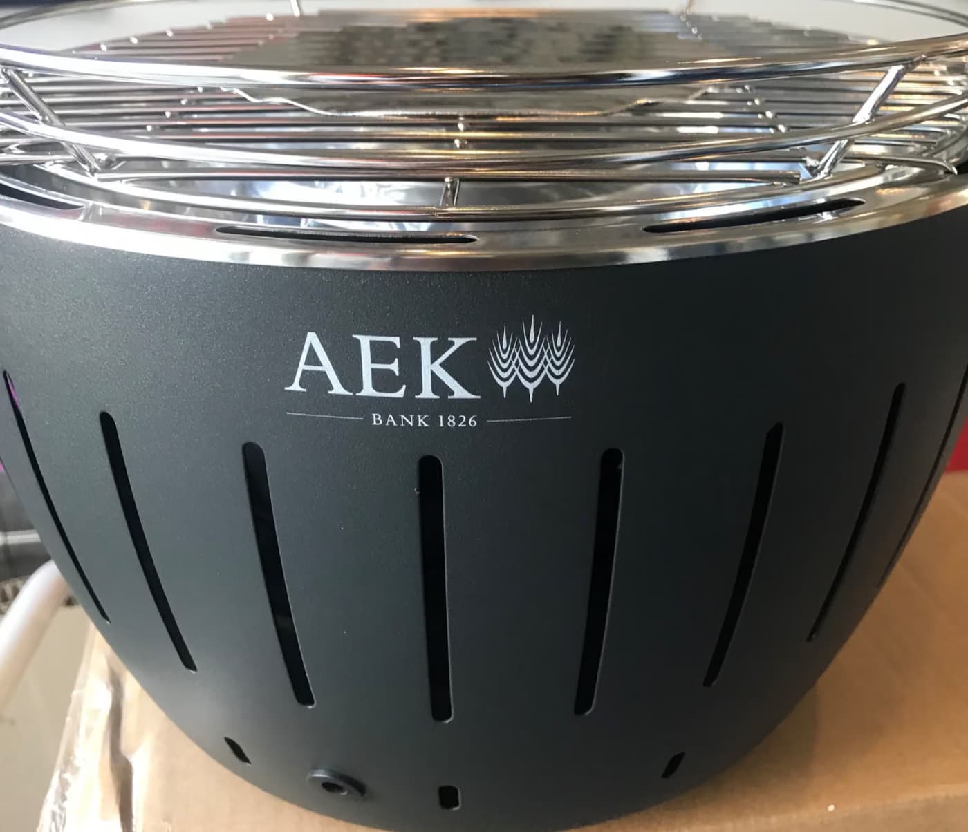 Weisses Logo der AEK BANK 1826 auf einem Holzkohle-Tischgrill